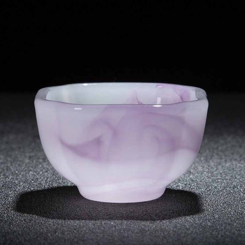 A small rounded cup made of translucent pale purple and white material, photographed against a black background on a dark textured surface.