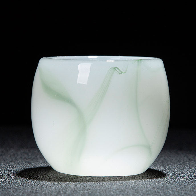 A small translucent white glass cup with pale green marbled veining, photographed on a dark textured surface against a black background. A red and white text strip appears along the bottom with product specifications in Chinese.
