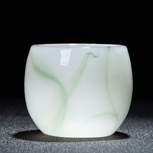A small translucent white glass cup with pale green marbled veining, photographed on a dark textured surface against a black background. A red and white text strip appears along the bottom with product specifications in Chinese.