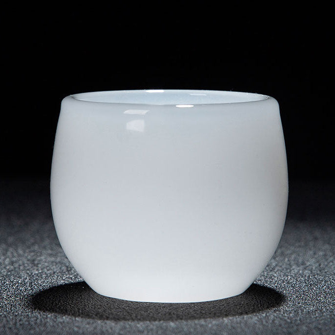 A small white glass cup with a smooth matte finish, photographed on a dark textured surface against a black background. A red and white text banner is visible along the bottom edge with Chinese dimensions and capacity details.