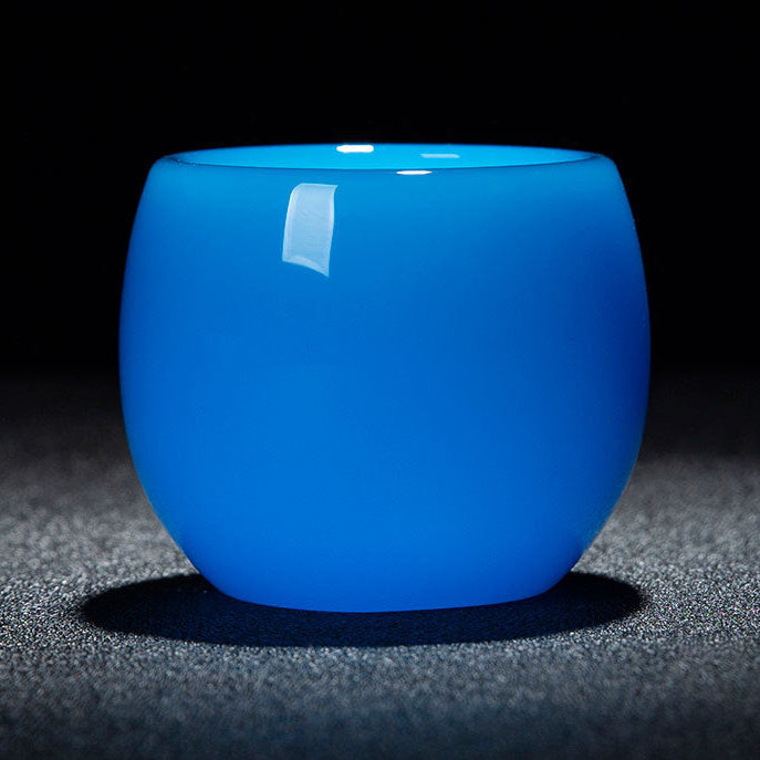A glossy translucent blue glass cup with a rounded shape, shown on a dark textured surface against a black background. A red and white text banner is overlaid at the bottom with dimensions and capacity details.
