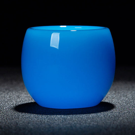 A glossy translucent blue glass cup with a rounded shape, shown on a dark textured surface against a black background. A red and white text banner is overlaid at the bottom with dimensions and capacity details.