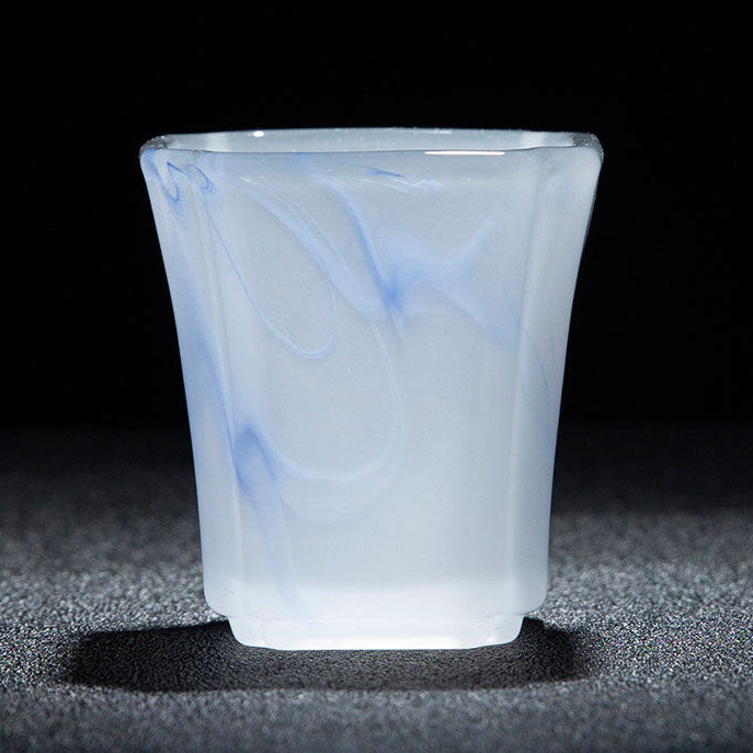 A frosted glass cup with a milky white body and delicate light blue marbled swirls, shown on a dark textured surface with a black background. A white and red text banner is visible at the bottom with Chinese characters describing the cup's dimensions and capacity.