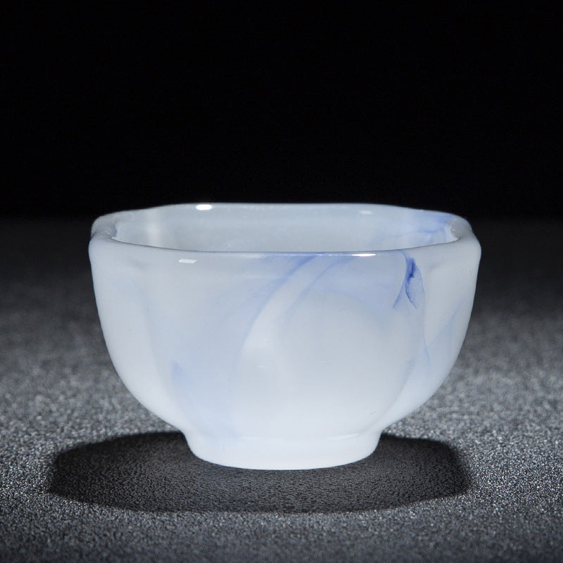 A small translucent white cup with subtle blue marbled veining, photographed on a dark textured surface against a black background.