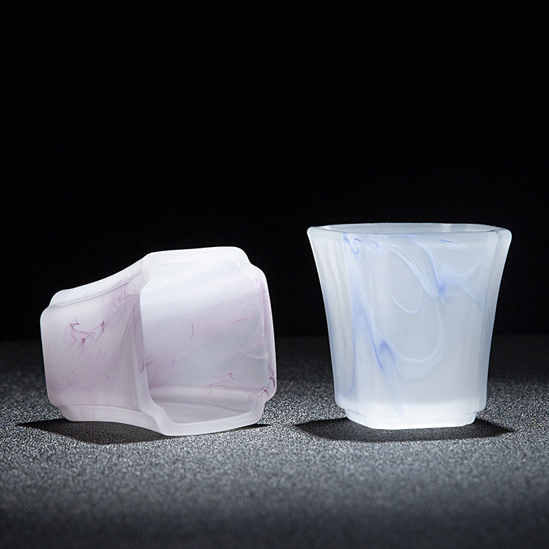 Two translucent frosted silicone cups with marble-like swirls, one pale pink and one pale blue, displayed on a dark textured surface against a black background.