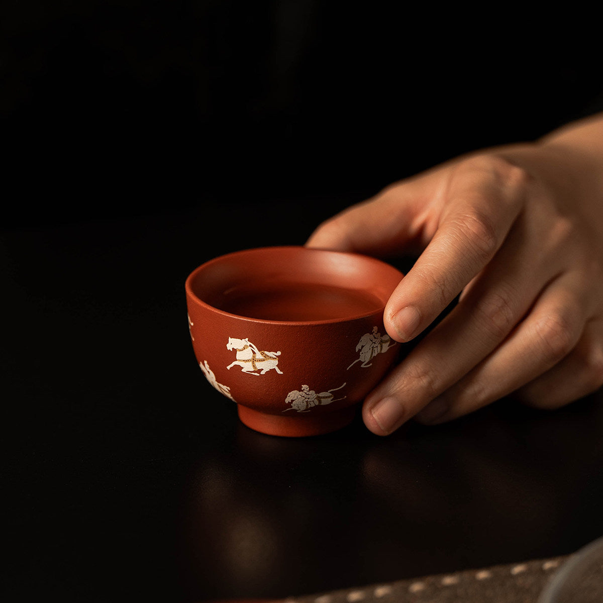 Hand holding a Zhu Ni clay master cup with silver horse motifs