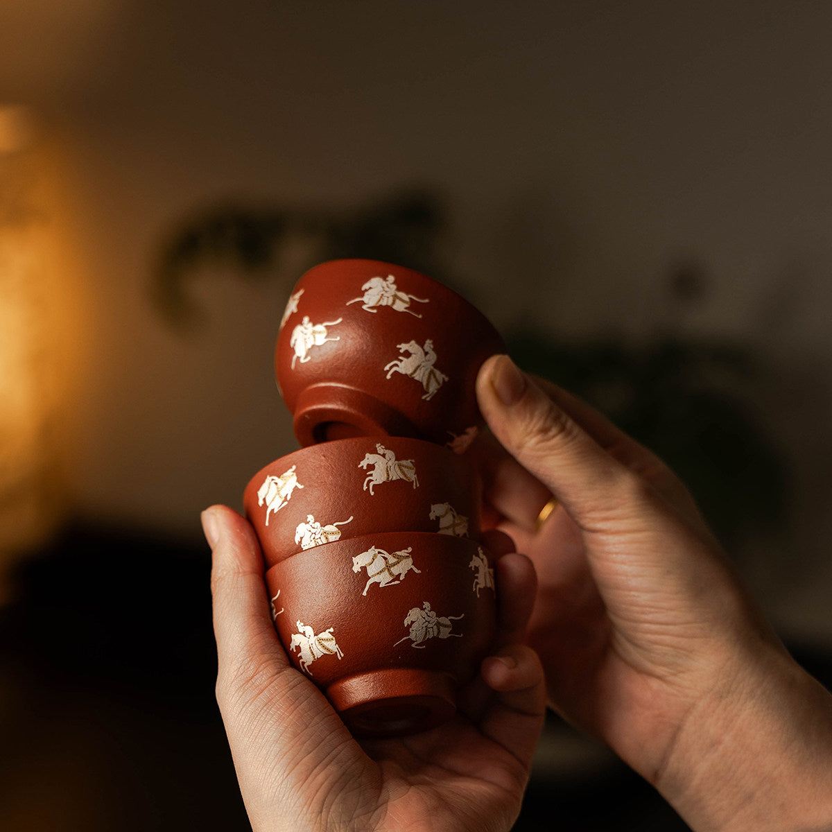 Three Zhu Ni clay tasting cups with horse-and-rider motifs held in hand