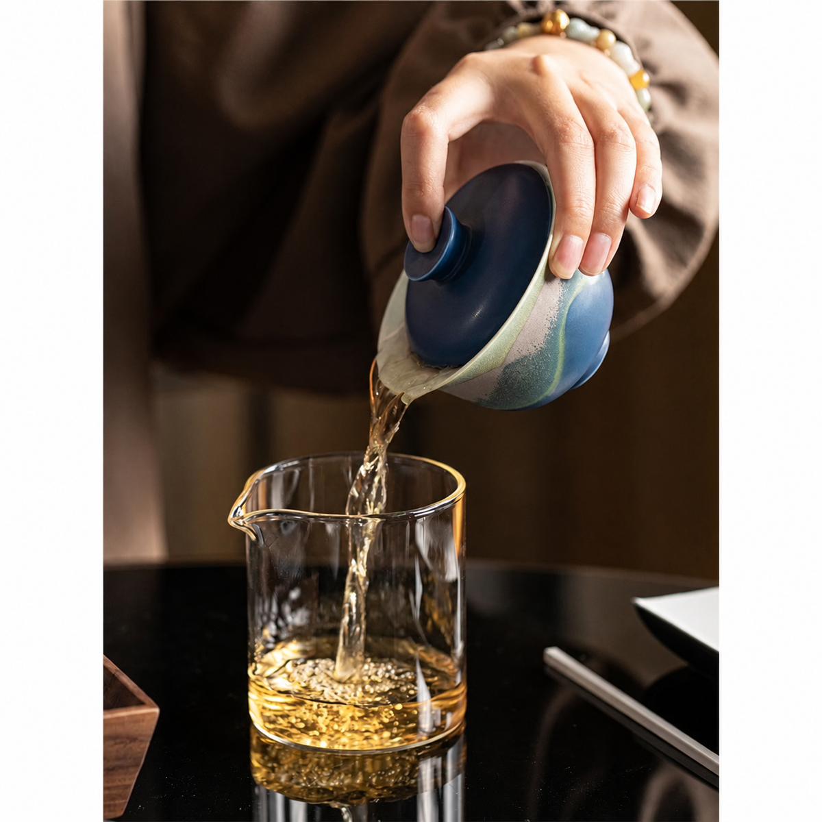 Blue mountain-glaze gaiwan pouring tea into a glass pitcher