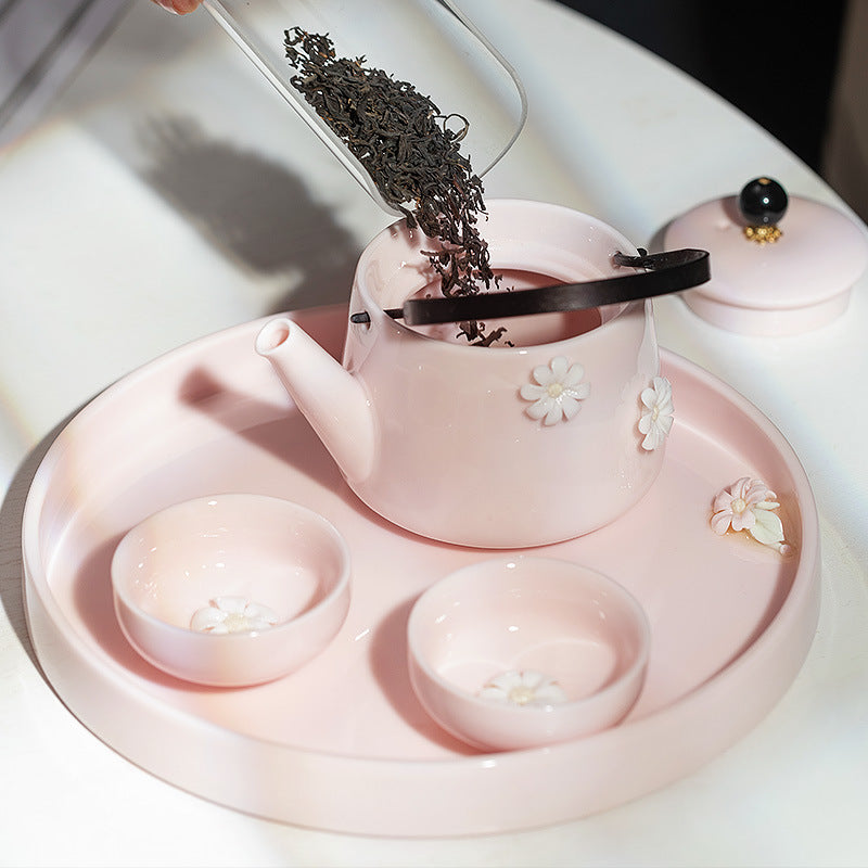 Loose tea being added to a blush pink floral ceramic teapot with two teacups